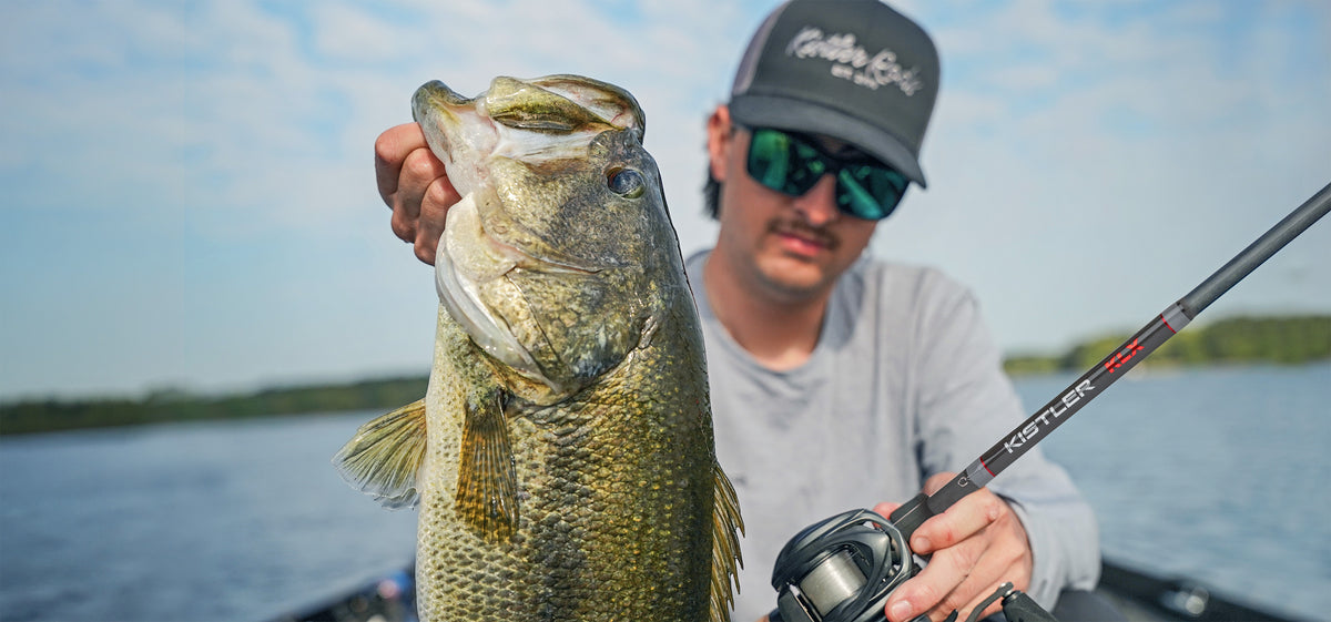 An angler on a boat holding a largemouth bass, a Kistler KLX rod and baitcasting reel in his other hand