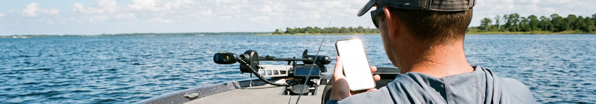 An angler sitting in the seat of a bass boat, checking his phone with a rod on the deck beside him